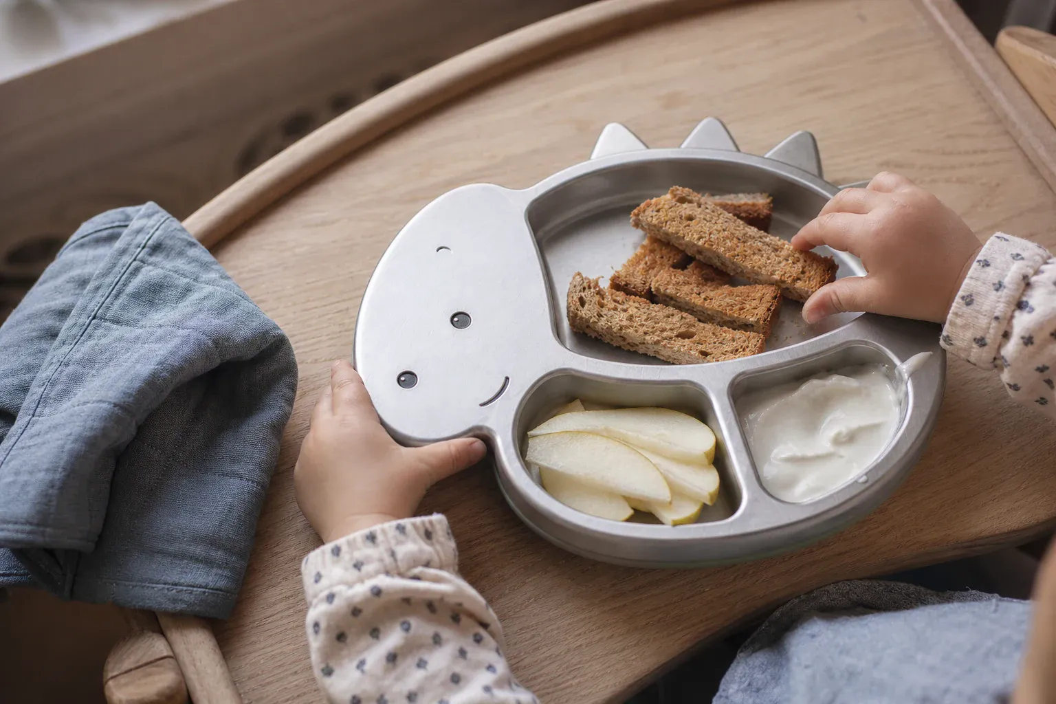 The dinosaur plate on an oak high-chair tray with toast, pear and yoghurt.